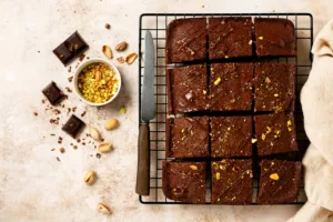 Chocolate squares with pistachio nuts and strawberries on a metal stand on a light stone background, top view, horizontal composition. Flat lay