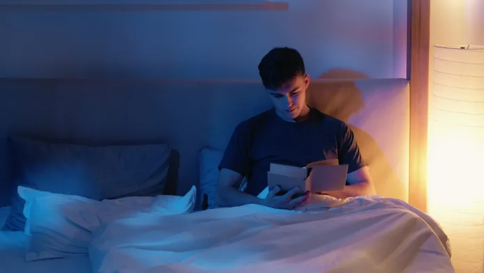 Peaceful man enjoying reading book in bed with warm soft lighting in intimate bedroom setting.