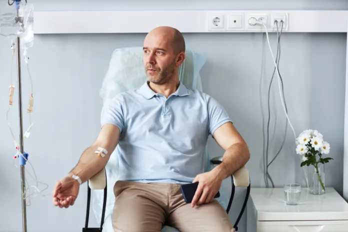 Portrait of adult man sitting in comfortable chair with IV drip during treatment session in clinic