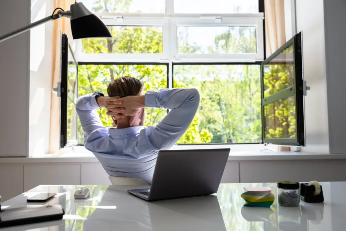 Relaxed Young Businessman Relaxing On Chair Behind Desk At Office