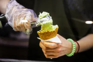 seller in disposable gloves put pistachio ice cream in a waffle cup.