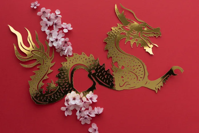 Chinese New Year. Dragon cut out in gilt paper with plum blossom decoration on red background. Copy space. Top view.