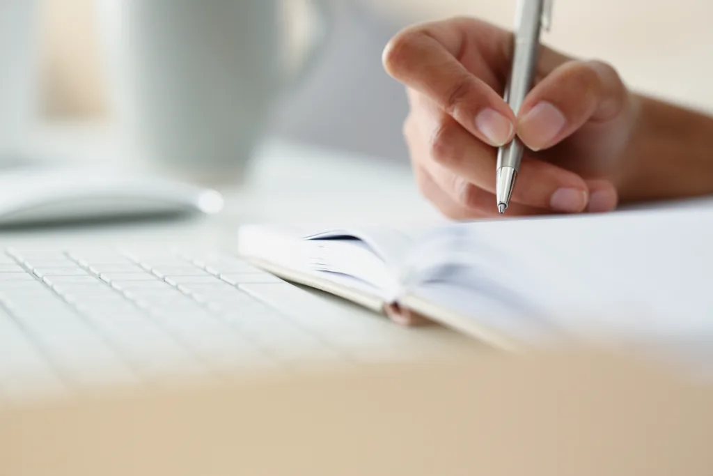 Close-up of persons hand writing down ideas in diary, notes for future, planning day in advance. Write with silver pen. Journal, creativity, writer concept