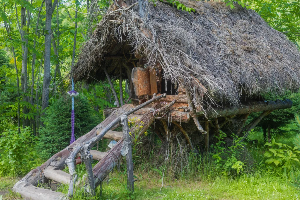 Kamlak, Altai Republic, Russia - June 13, 2024: Baba Yaga's small hut from wood and branches and standing on stylizated chicken legs among summer forest in the Gorno-Altaysk Botanical Garden.