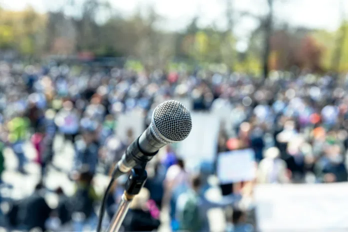 Protest or public demonstration, focus on microphone, blurred crowd of people in the background